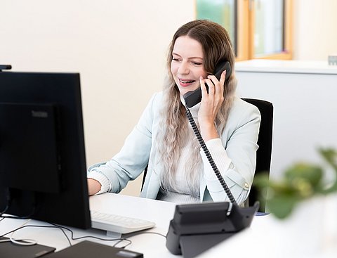 EIne Frau sitzt vor einem Computer und telefoniert.