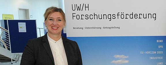 Klarita Nestler, Abteilungsleiterin Forschungsförderung, vor einem Aufsteller mit der Aufschrift UW/H-Forschungsförderung