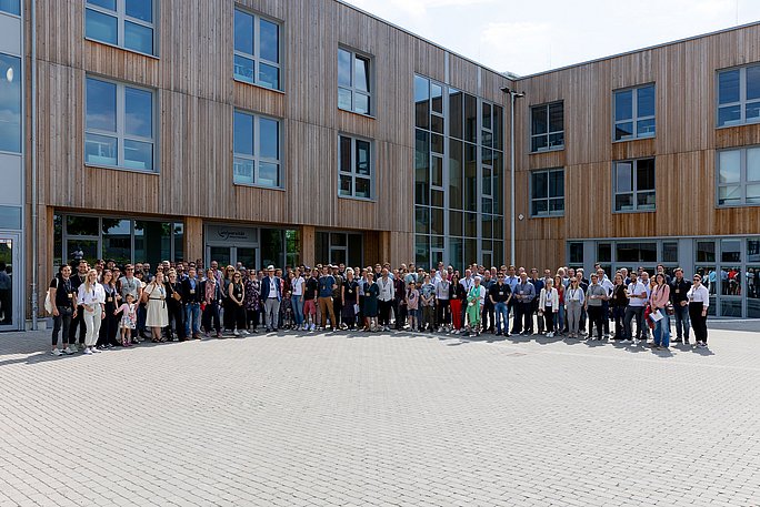 Eine große Personengruppe posiert vor einem Holzgebäude.