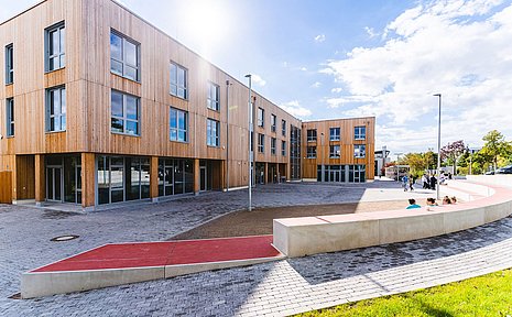 Bild eines Holzgebäudes mit Vorplatz in der Sonne