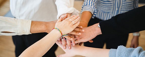 Mehrere Personen stehen im Kreis und legen ihre Händer übereinander.