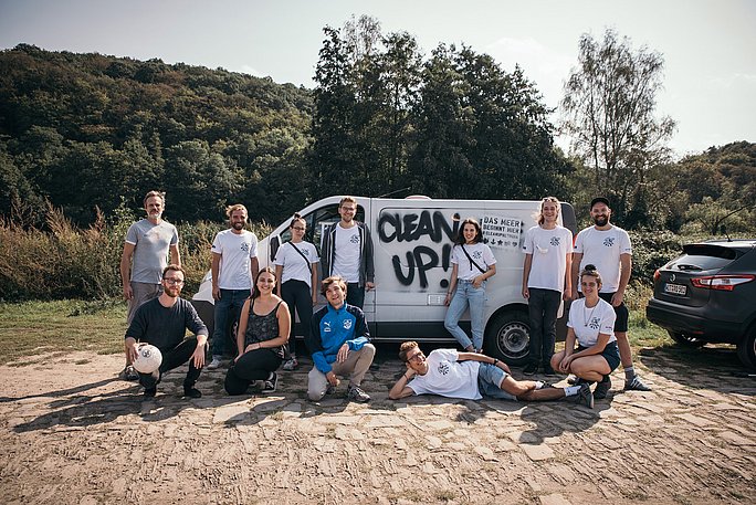 Engagierte Studierende posieren vor einem weißen Transporter, den die Aufschrift "Clean Up" ziert.