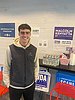 A young man stands in front of a table with campaign posters and flyers for presidential candidate Kamala Harris.