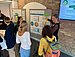 Participants stand in front of a metaplan wall with a poster and talk to Verena Timmer from ZNU.