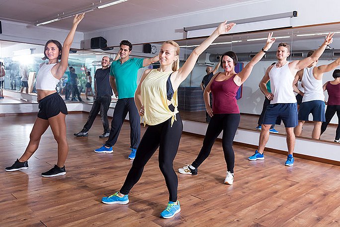 Eine Gruppe von Frauen und Männern tanzt in einer Sporthalle Zumba.