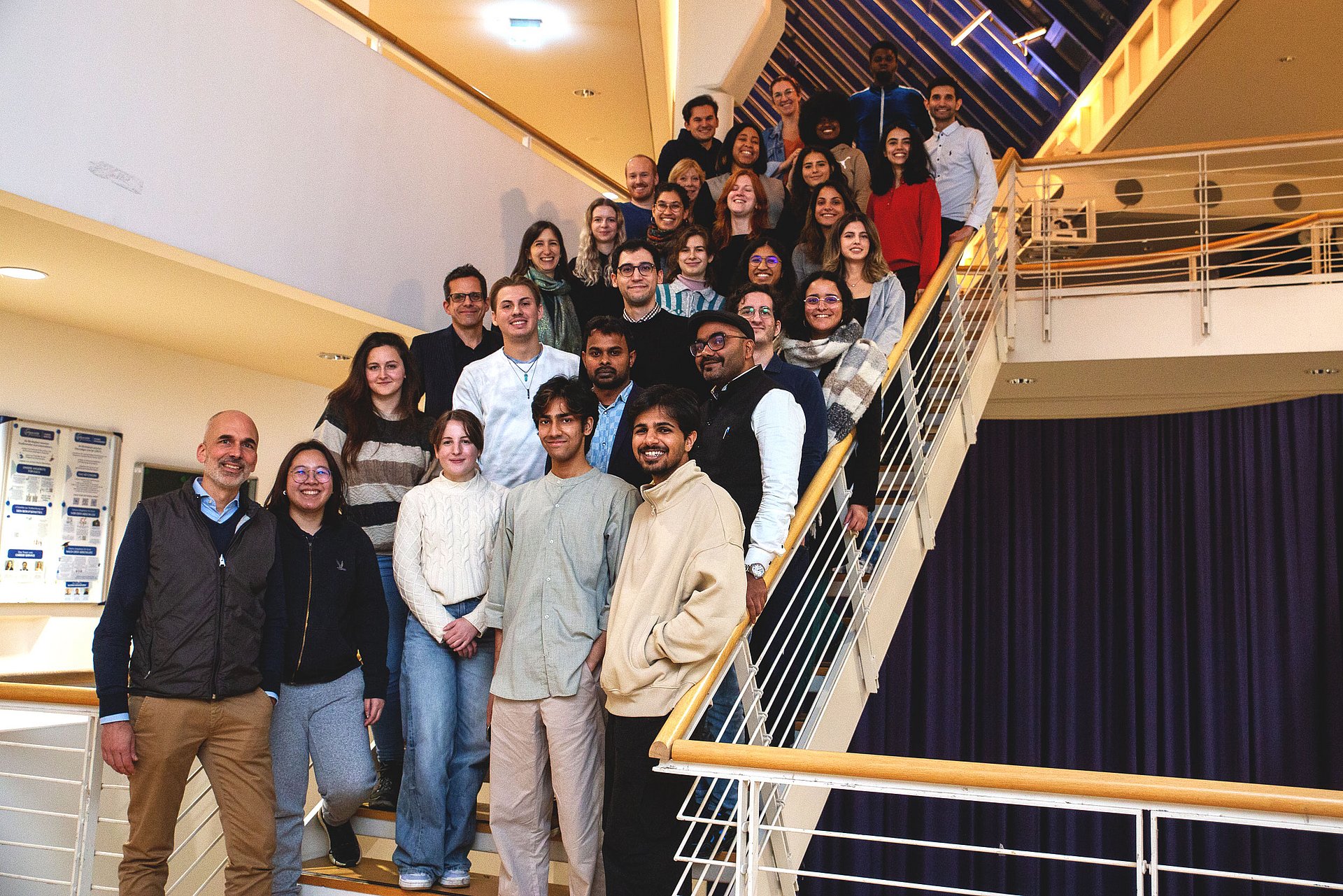 Eine Gruppe internationaler Studierenden posiert hintereinander aufgereiht auf einer Treppe für das Foto.