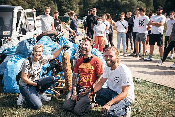 Menschen lachen in die Kamera, Müllbeutel im Hintergrund