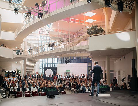 Blick von einer Bühne in eine große Halle, in der ein Publikum sitzt.