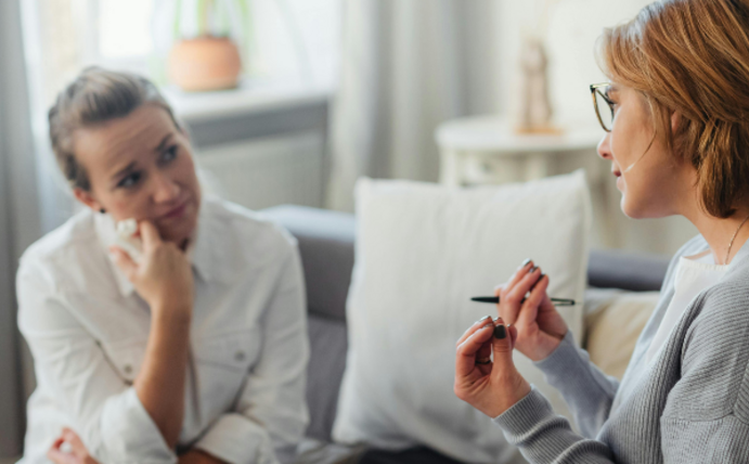 Zwei Frauen sitzen auf einer Couch und sind in ein Gespräch vertieft.