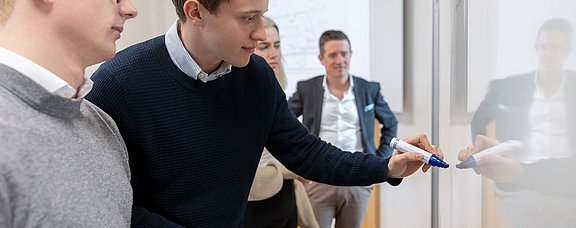 Zwei Studierende und ein Dozent erarbeiten ein Thema am Whiteboard.