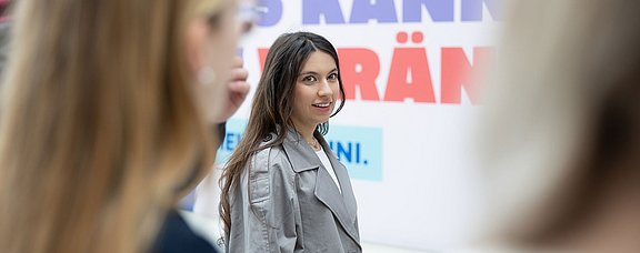 Eine Gruppe junger Frauen steht vor einem Plakat.