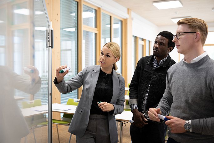 Eine Professorin erläutert zwei Studenten des Fachs Management & Psychologie (B. Sc.)  ein Thema am Whiteboard.