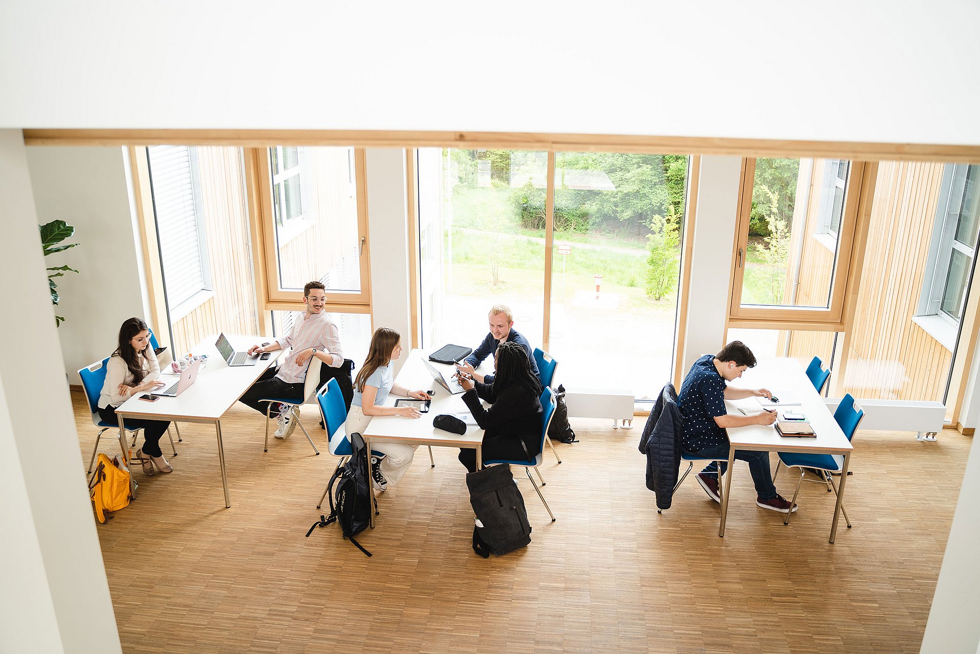 Sechs Studierende sitzen an drei Tischen verteilt, lernen und unterhalten sich.