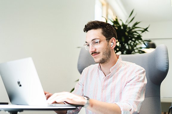 Ein Student sitzt in einem Sessel und schreibt an seinem Laptop.