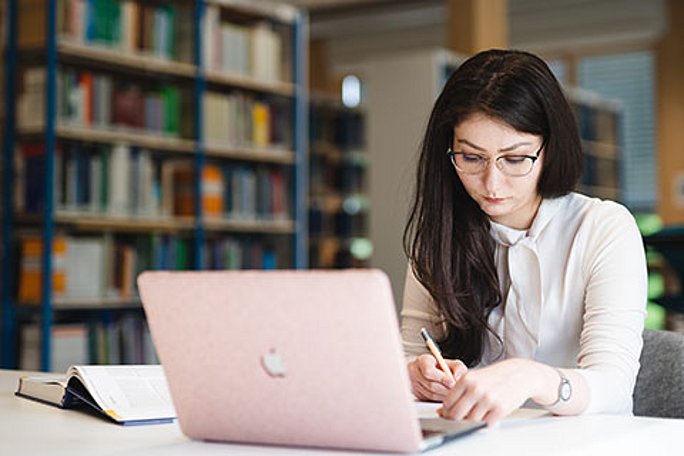 Eine Studentin sitzt mit ihrem Laptop in der Bibliothek und lernt 