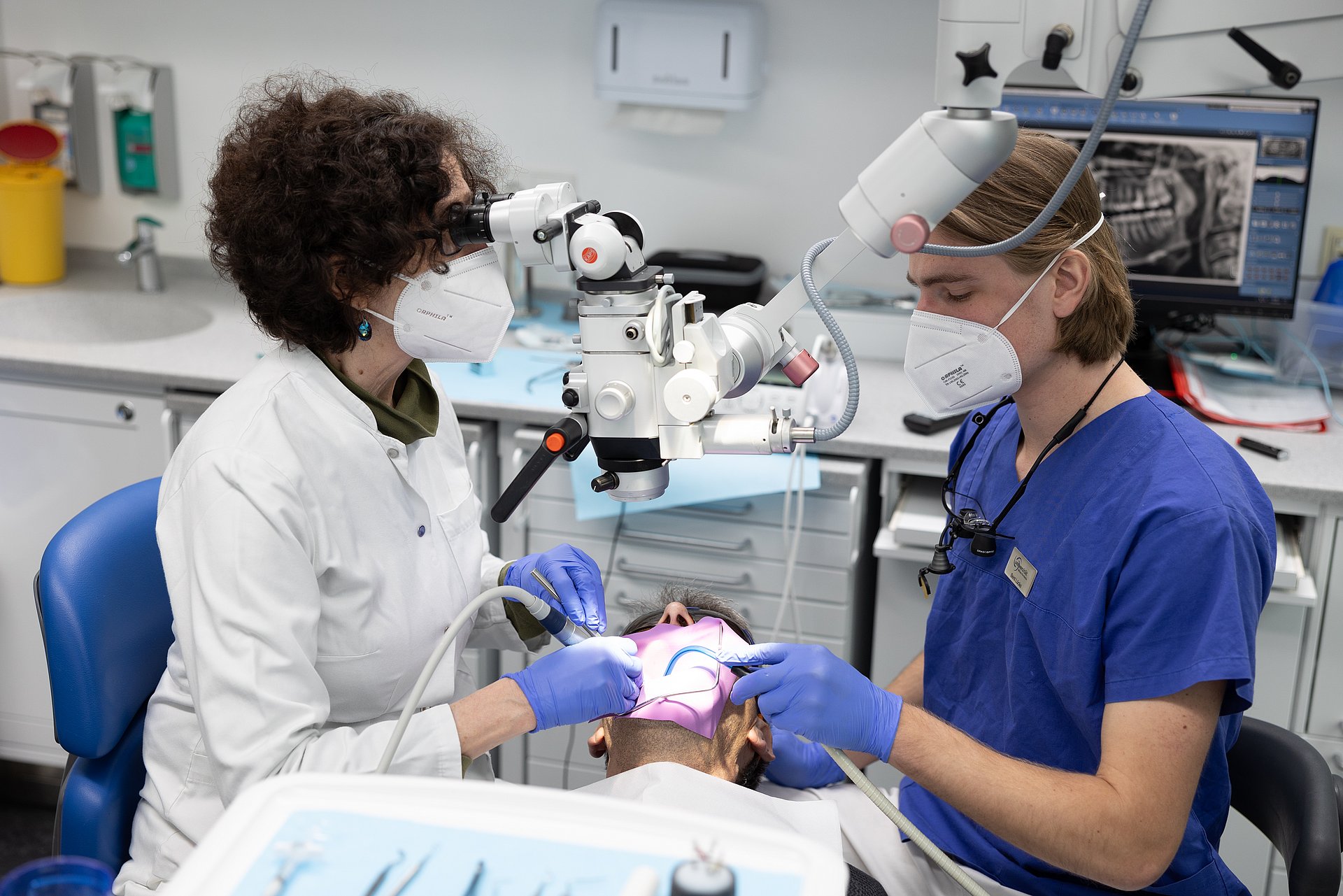 Eine Zahnärztin und eine Helferin behandeln einen Patienten.