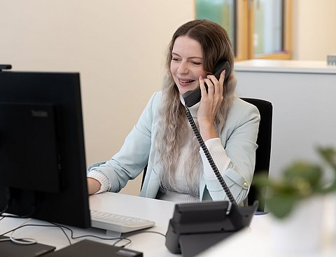 Eine Frau sitzt vor ihrem PC und telefoniert dabei.