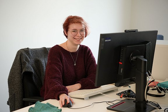 Eine junge Frau Sitz an einem Computerarbeitsplatz.