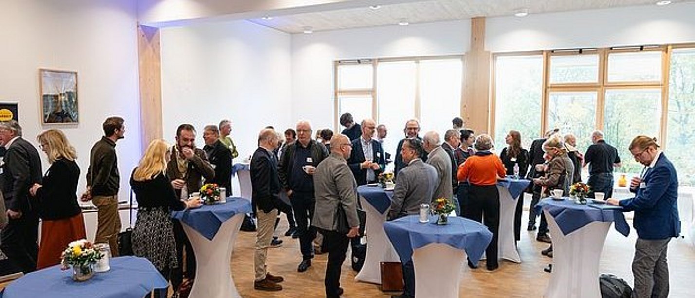 Personen unterhalten sich an Stehtischen in einem Foyer.