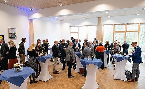 Personen unterhalten sich an Stehtischen in einem Foyer.