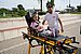 Girl lies with her stuffed animal on the stretcher of an ambulance.