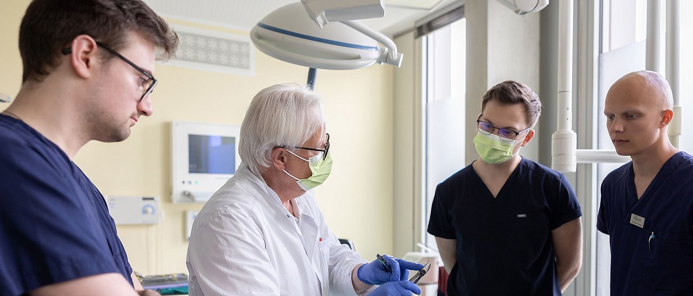 Ein Zahnmedizin-Professor erklärt drei Studierenden ein Gerät.