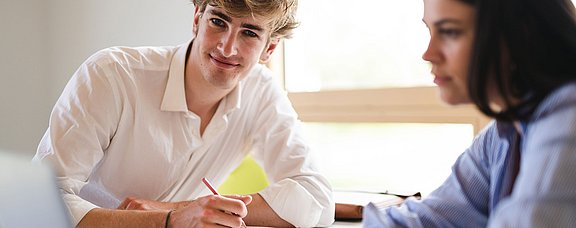 Ein junger Mann und eine junge Frau sitzen mit einem Laptop an einem Tisch.