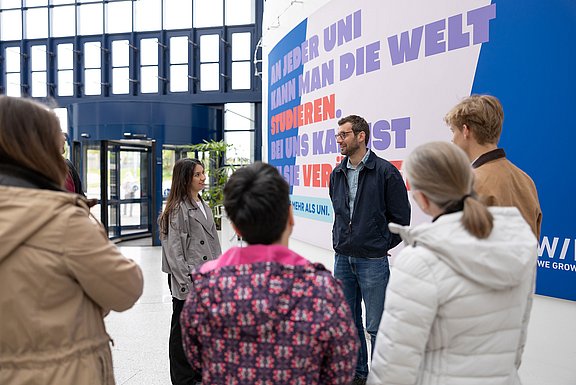 Eine Gruppe von sechs Personen steht im Kreis, ein Mann erklärt etwas.