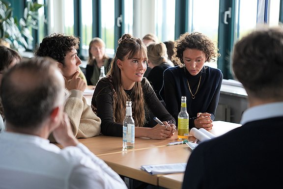 Studierende sitzen um einen Tisch und diskutieren.