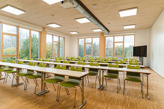 Interior shot of a brightly lit seminar room with rows of tables and chairs