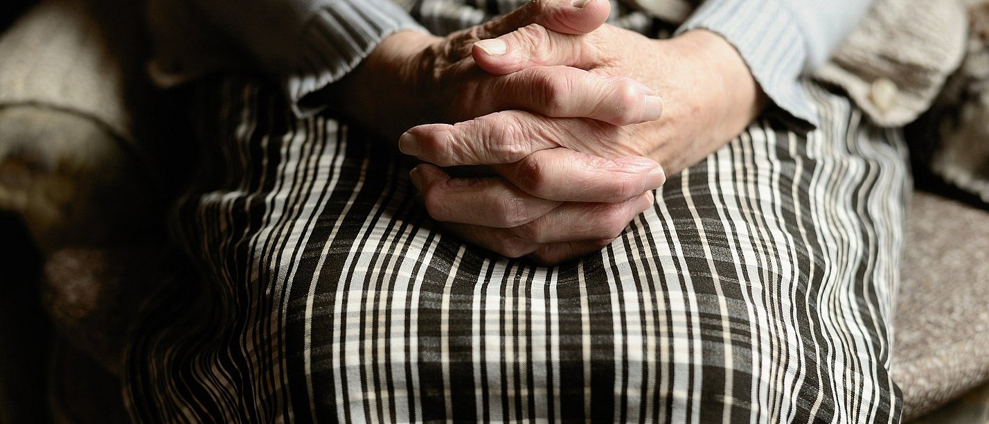 Two folded hands lie on a lap.