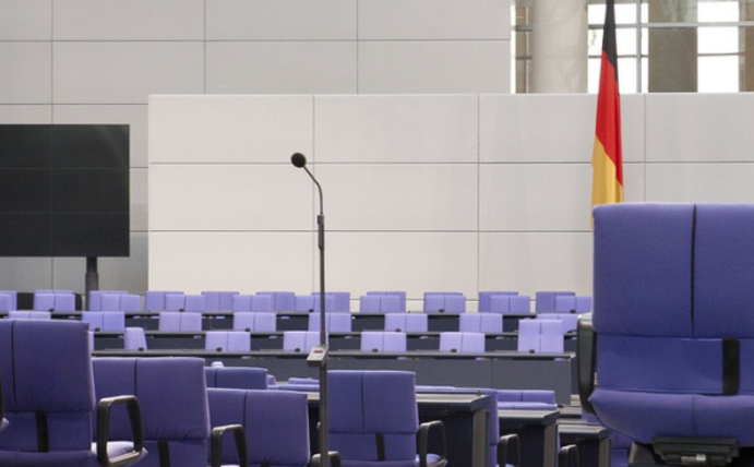 Blick auf die Sitze des leeren Bundestages. Im Hintergrund ist eine Deutschlandflagge.