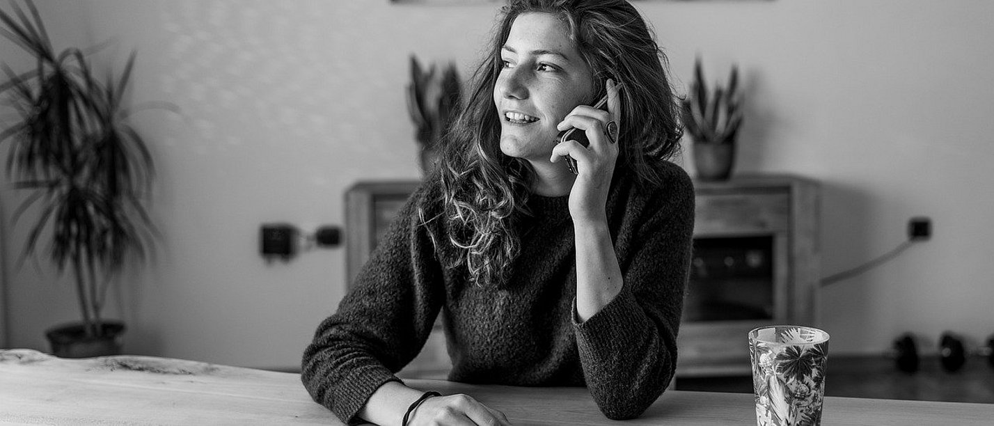 A young woman is sitting at a table talking on the phone.