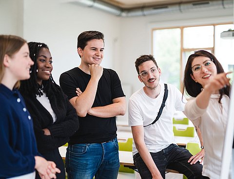 Eine Gruppe Studierender steht am Flipchart und diskutiert über ein Thema.