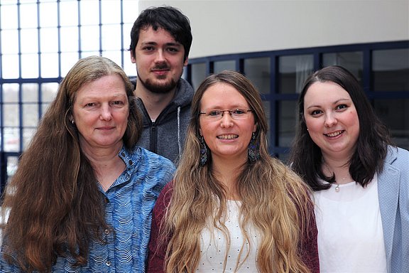 Vier Personen stehen nebeneinander und lächeln in die Kamera.