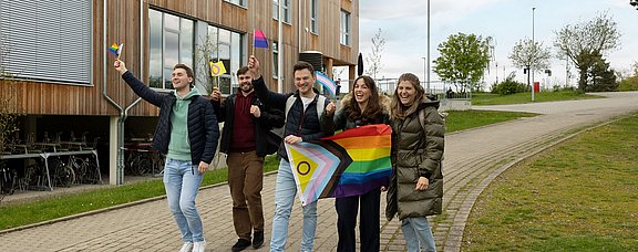 Studierende laufen mit geschwenkten Pride-Flaggen über den Campus.