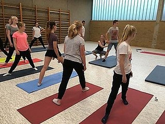 Schüler:innen machen in einer Turnhalle Bewegungsübungen auf Matten.