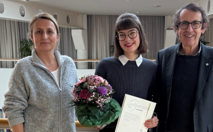 Drei Personen stehen nebeneinander in der Universität. In der Mitte Theresa Busse, eine junge Frau, die ihre Berufungsurkunde und einen Blumenstrauß in der Hand hält und glücklich aussieht. Links von ihr Prof. Dr. Margareta Halek, rechts Prof. Dr. Stefan Zimmermann.