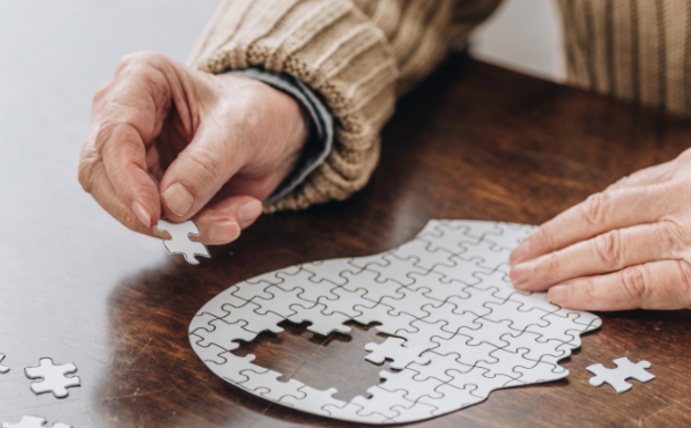 Hände einer älteren Person puzzeln einen Kopf zusammen als Symbolbild für Demenz