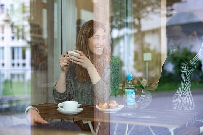 Eine Studierende macht Pause im Café Larix auf dem Campus der UW/H und trinkt Kaffee.