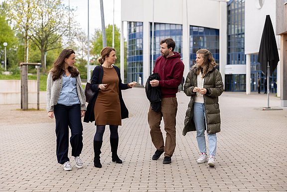 Eine Gruppe Studierender läuft über den Uni-Campus und unterhält sich dabei.