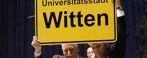 Mann hält Ortsschild von Witten hoch: Universitätsstadt Witten