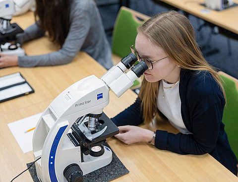 Studentin schaut durch ein Mikroskop