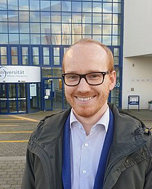 Portrait eines Mannes vor dem Hauptgebäude der Uni Witten/Herdecke.