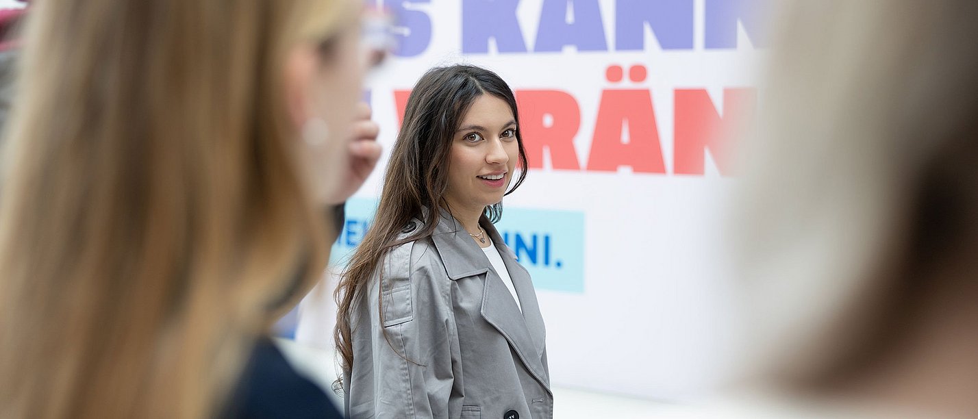 Eine Gruppe junger Frauen steht vor einem Plakat.