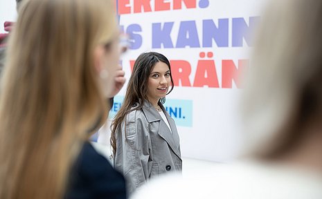 Eine Gruppe junger Frauen steht vor einem Plakat.