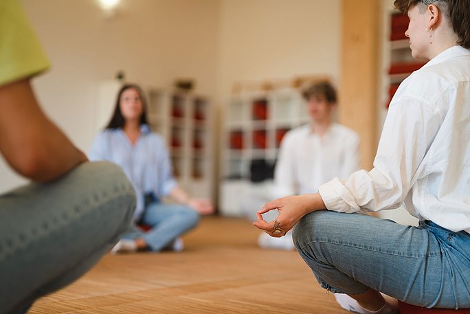 Studierende sitzen auf dem Fußboden im Yogakurs.