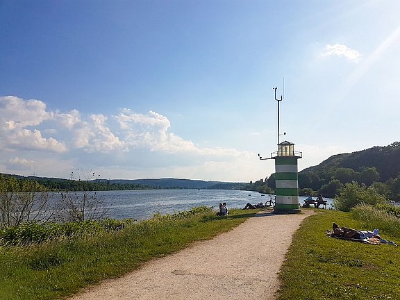 Foto eines Spazierwegs am See mit Blick auf einen kleinen Leuchtturm.