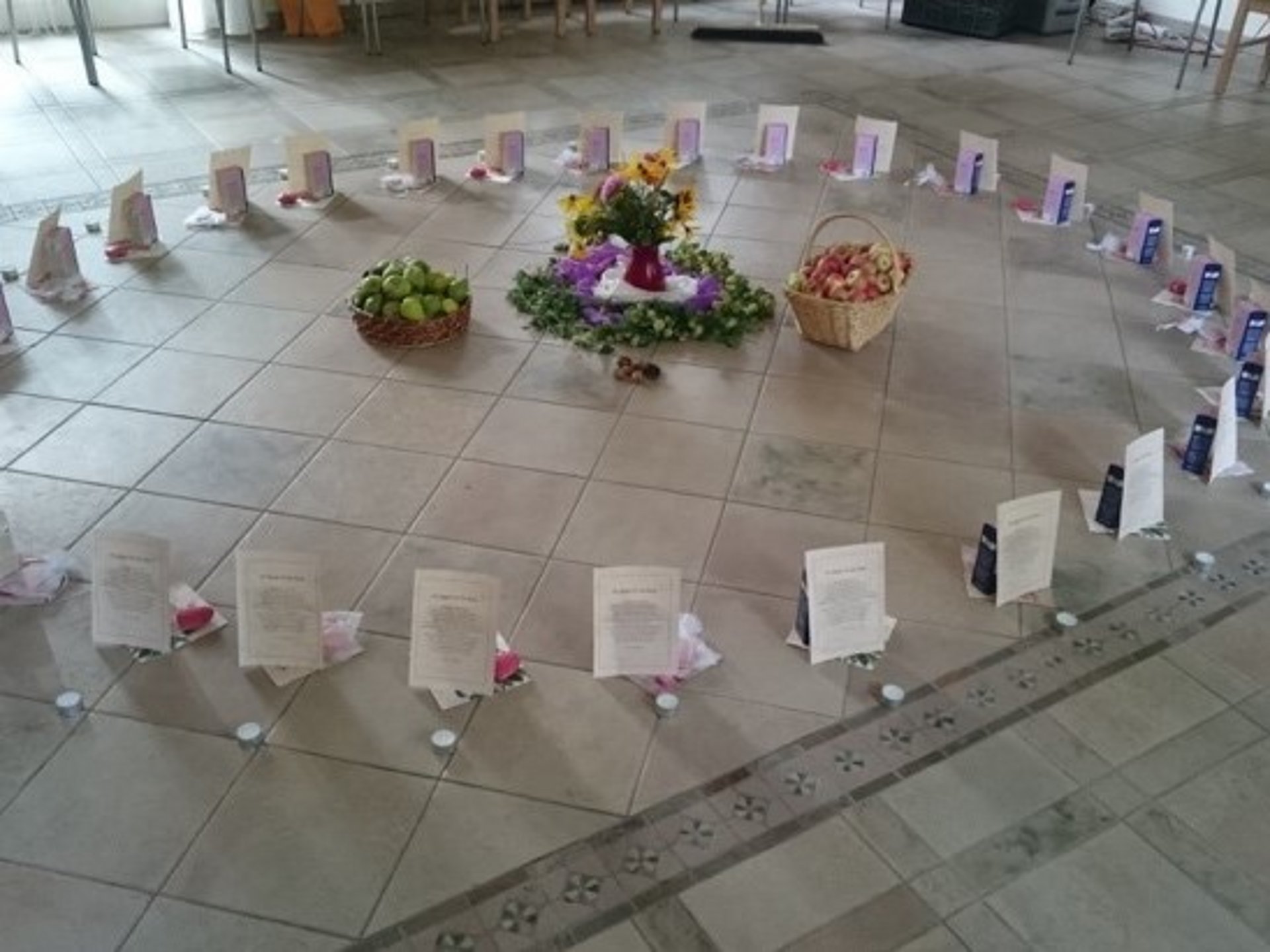 In der Mitte eines Kreises aus Teelichtern und Papieraufstellern stehen Blumen und zwei Körbe mit Obst.