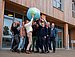 Many people hold an inflatable globe in the air together and smile at the camera.